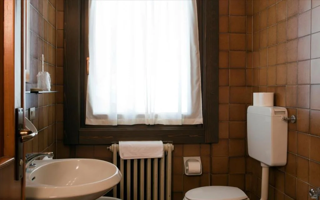 Bagno con lavabo, WC e finestra con tenda, piastrelle marroni