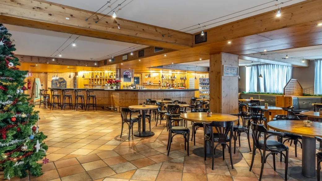 Sala bar dell'hotel con tavoli rotondi, sedie in legno, bancone e albero di Natale addobbato