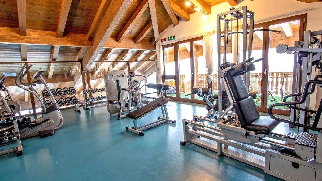 Palestra dell'hotel con attrezzi fitness, pesi e soffitto in legno con travi a vista