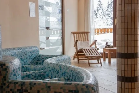 Zona benessere con sedute in mosaico colorato e sdraio in legno davanti alla finestra sulla neve