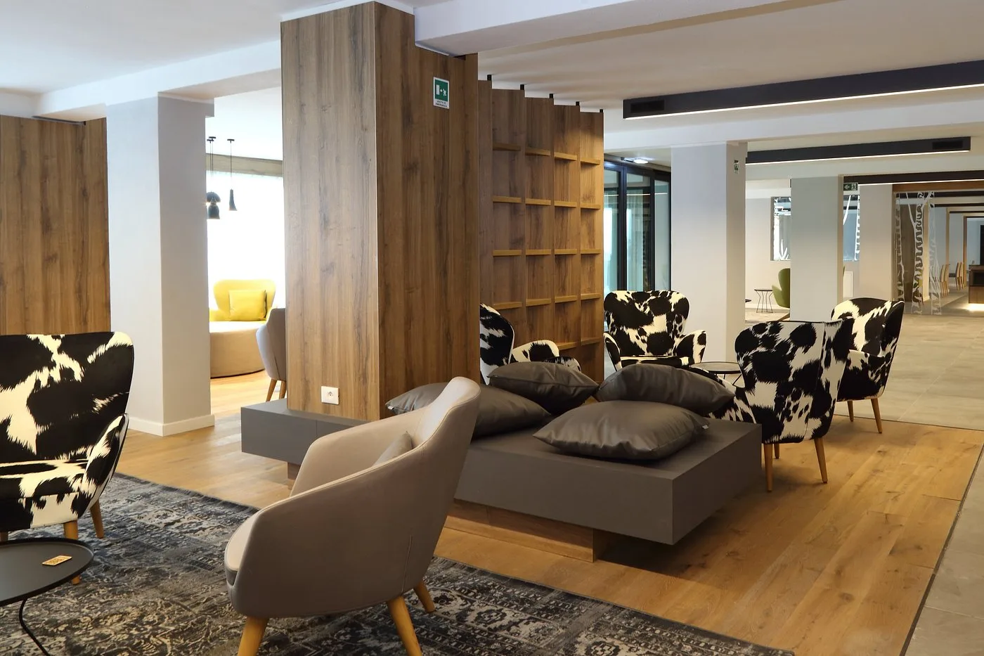 Area comune con poltrone fantasia mucca, divano grigio e libreria in legno