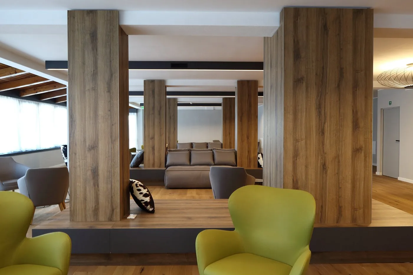Zona lounge con colonne in legno, divano grigio e poltrone verdi