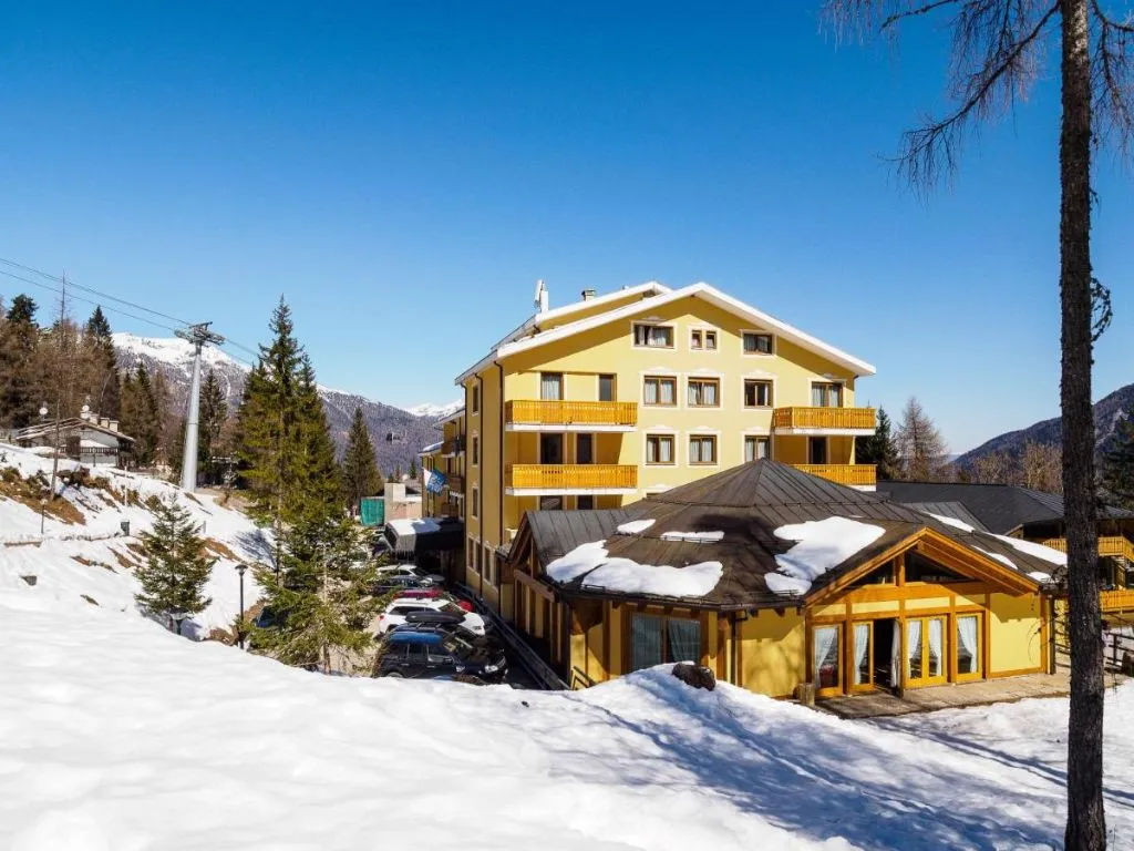 Esterno dell'hotel circondato dalla neve con piste da sci e montagne sullo sfondo