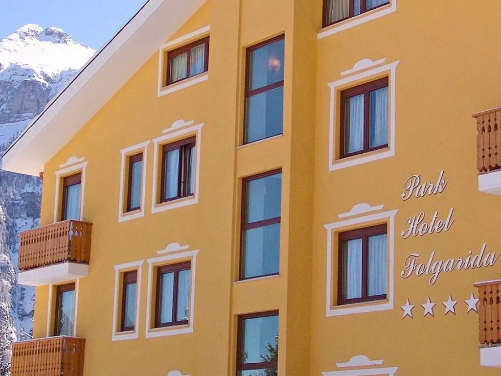 Facciata gialla del Park Hotel Folgarida quattro stelle con montagne innevate