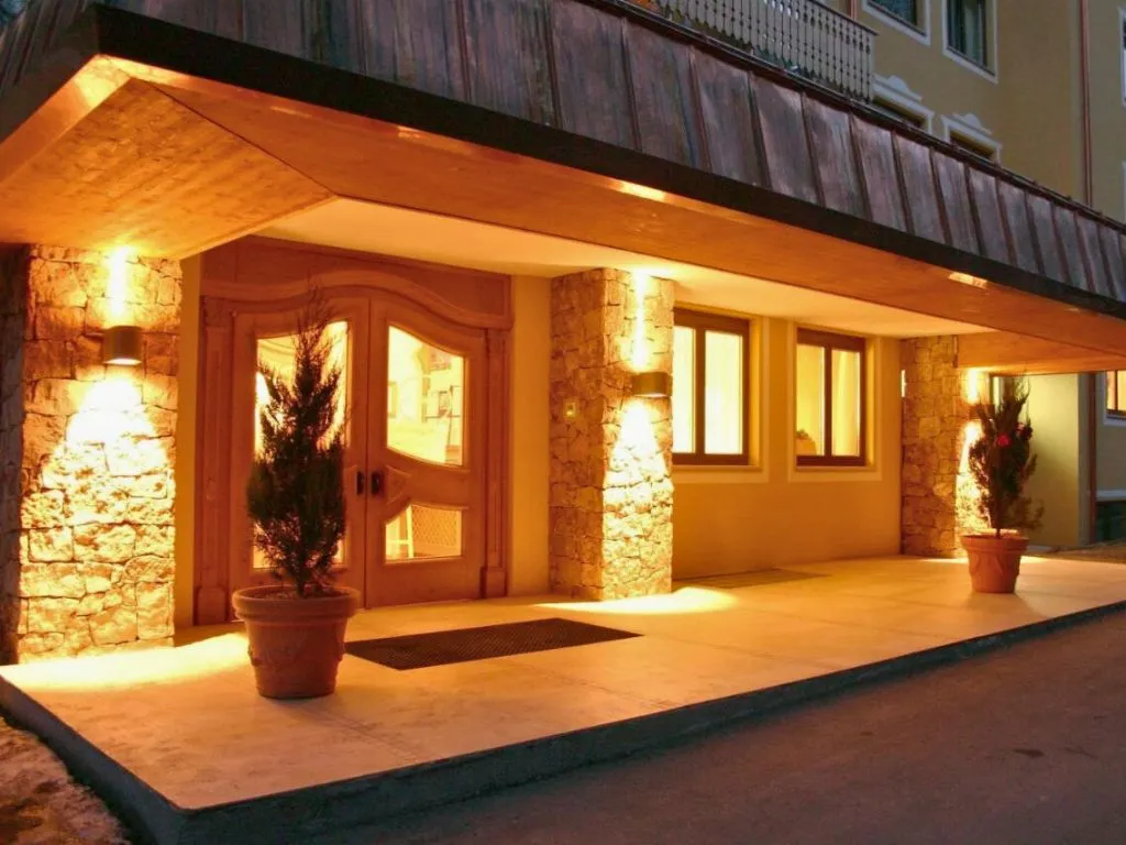Ingresso dell'hotel illuminato di sera con colonne in pietra e portone in legno