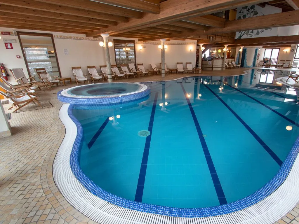 Piscina interna con vasca idromassaggio, colonne e lettini lungo il bordo