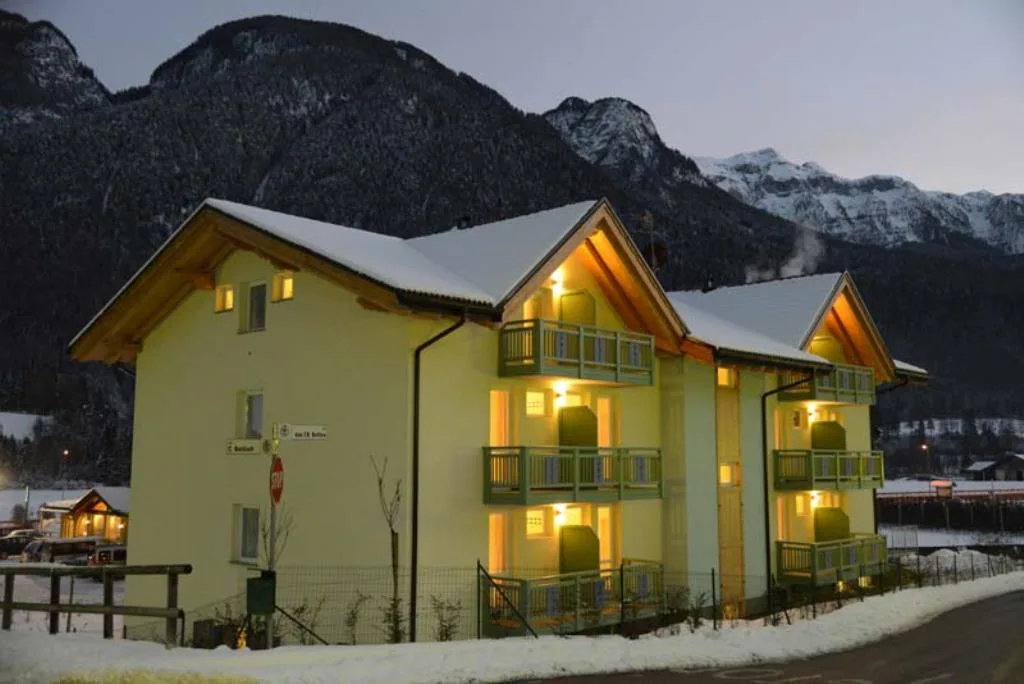 Esterno dell'hotel illuminato di sera con montagne innevate sullo sfondo