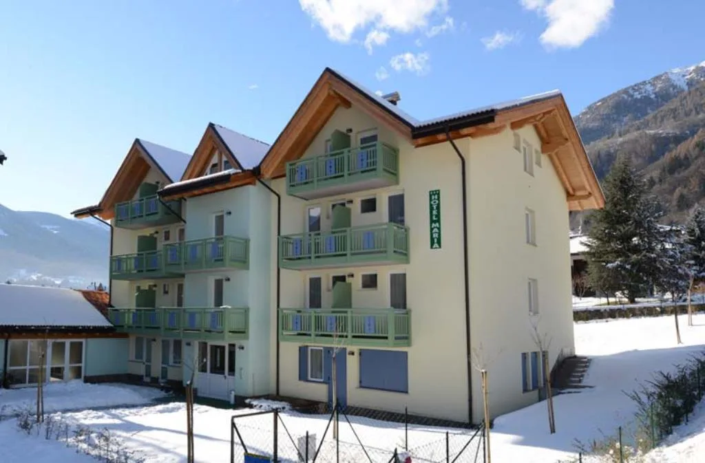 Veduta diurna dell'Hotel Maria con balconi verdi e cielo azzurro tra le montagne innevate