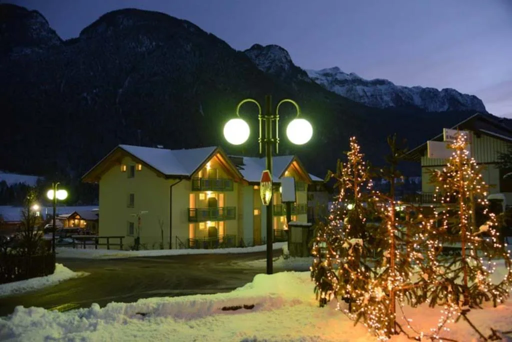 Vista notturna dell'hotel con lampione e alberi addobbati con luci natalizie sulla neve
