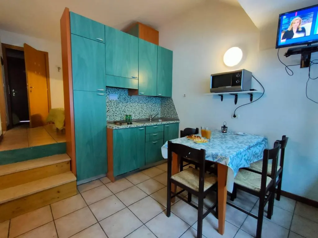 Cucina compatta verde con tavolo da pranzo, microonde e TV