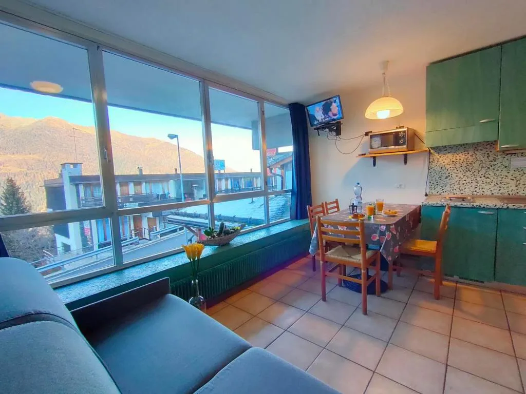 Soggiorno con divano, cucina verde e ampia vetrata panoramica sulle montagne
