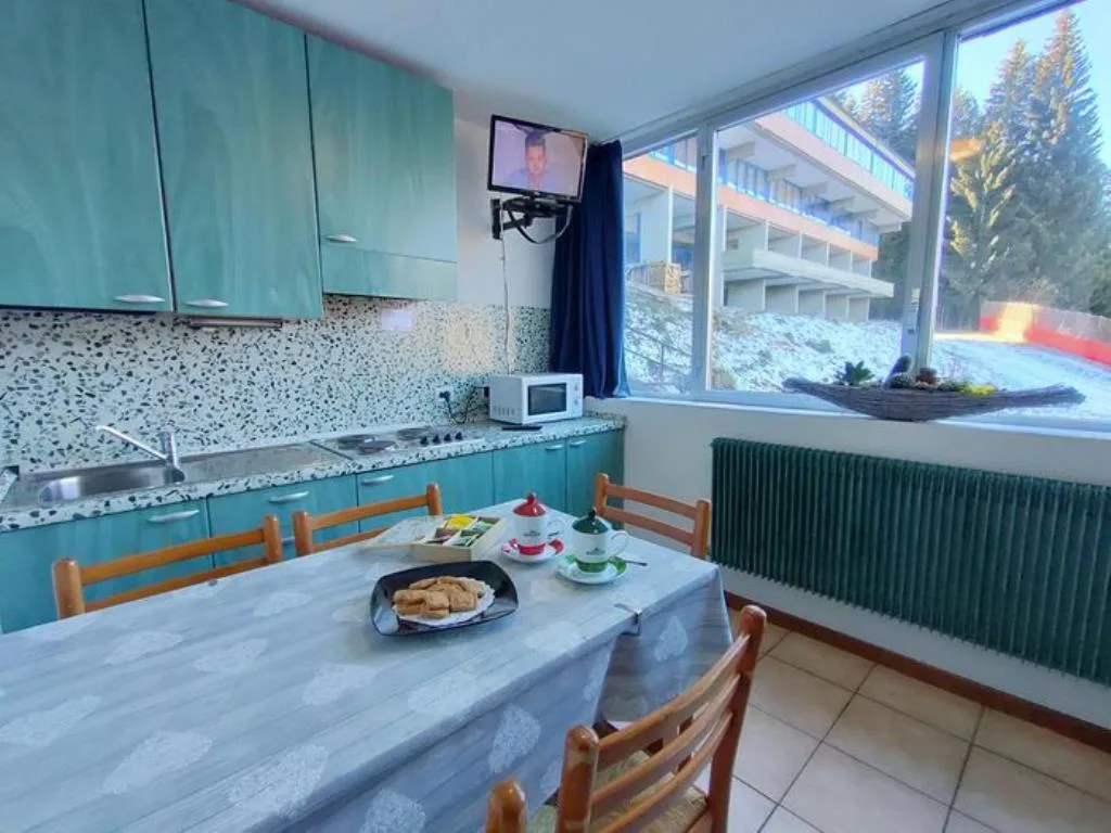 Cucina verde con tavolo apparecchiato, microonde e finestra sul giardino innevato