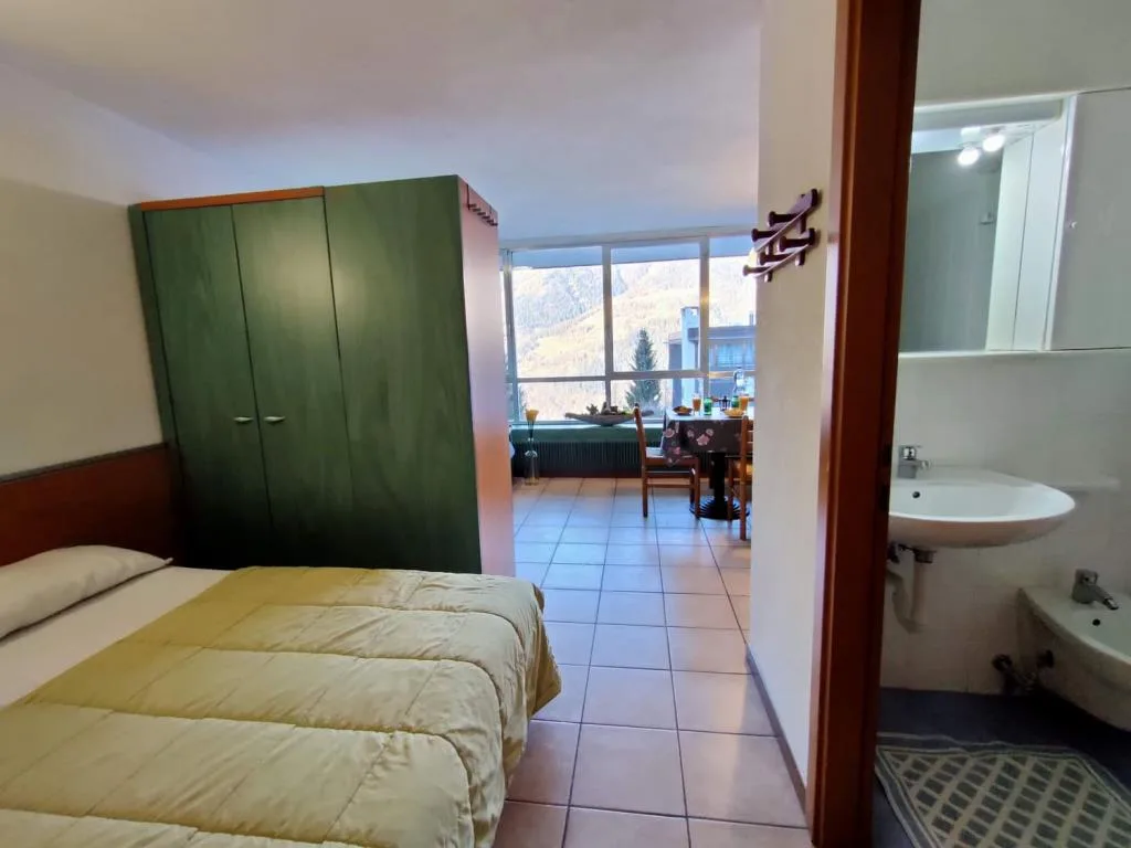 Camera con letto matrimoniale, armadio verde, zona pranzo e bagno adiacente