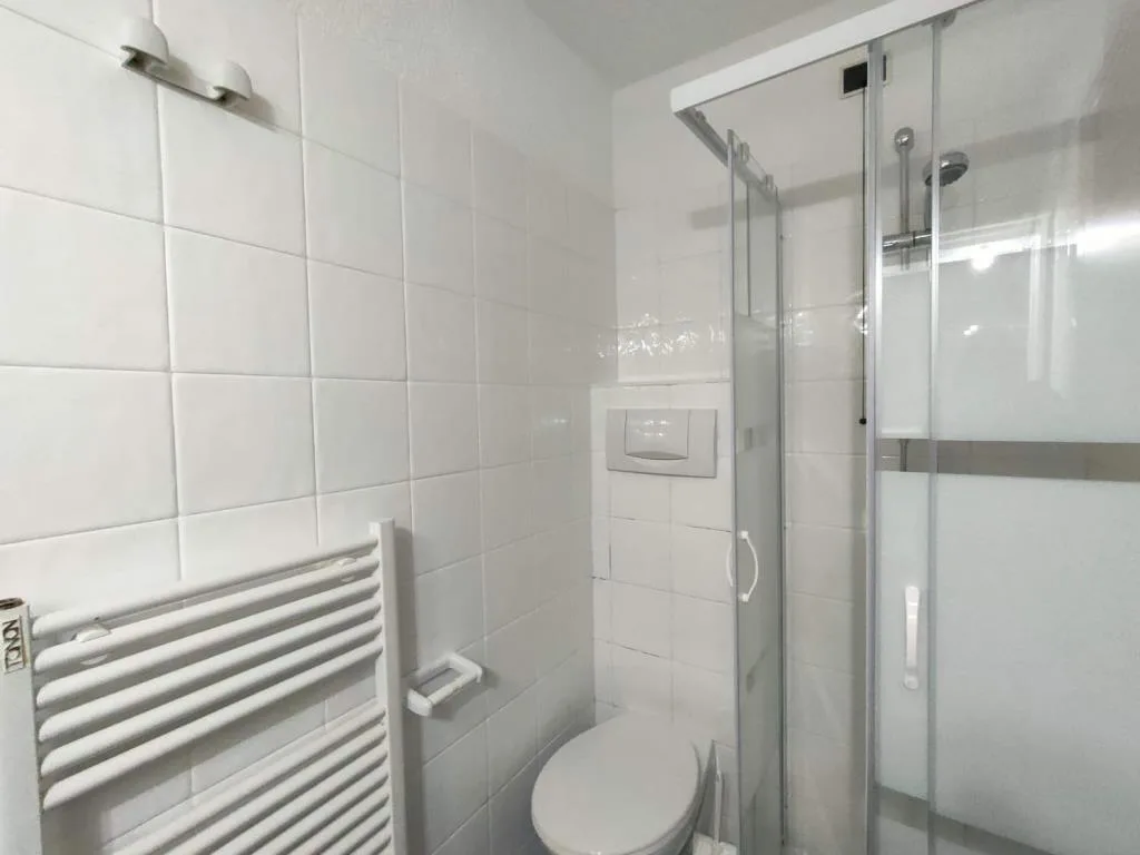 Bagno con doccia, WC e termoarredo bianco su piastrelle chiare