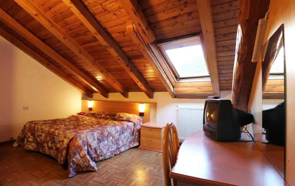 Camera mansardata con soffitto in legno a vista, letto matrimoniale e finestra lucernario