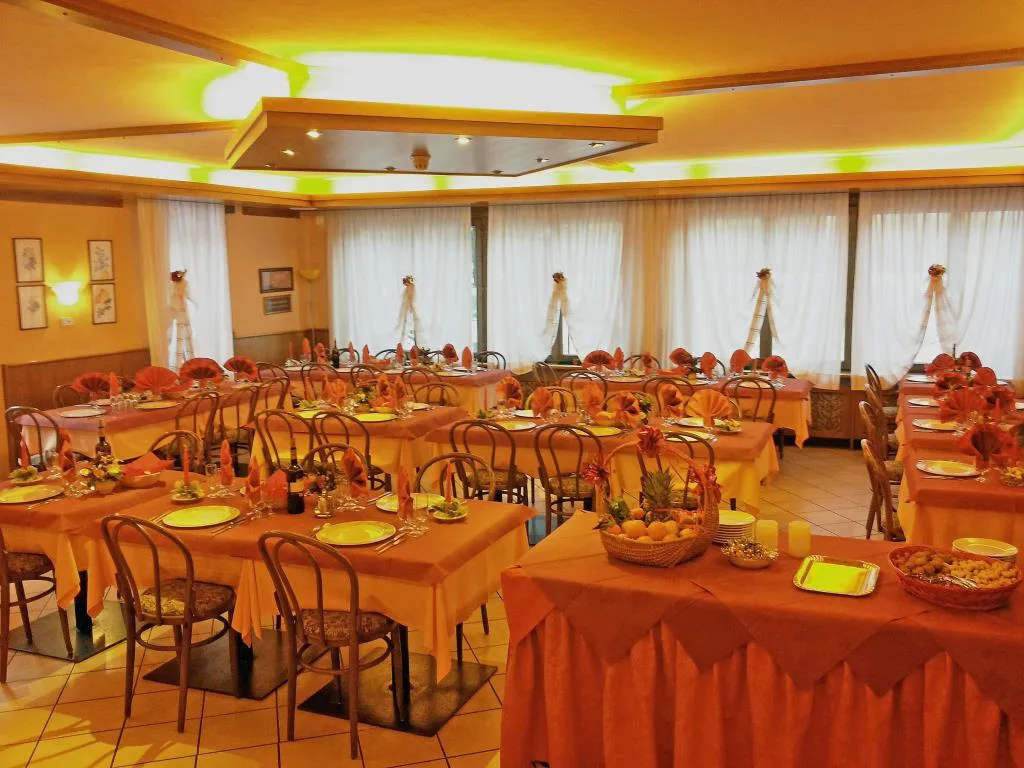 Sala ristorante apparecchiata a festa con tovaglie arancioni e tovaglioli decorati