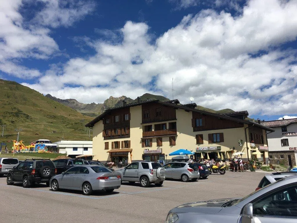 Esterno dell'hotel di montagna con parcheggio auto e vetta verde sullo sfondo