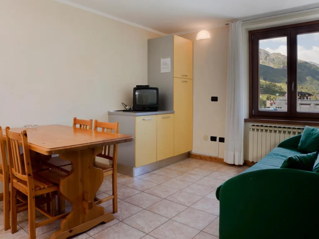 Soggiorno con tavolo in legno, divano verde, TV e finestra con vista montagna